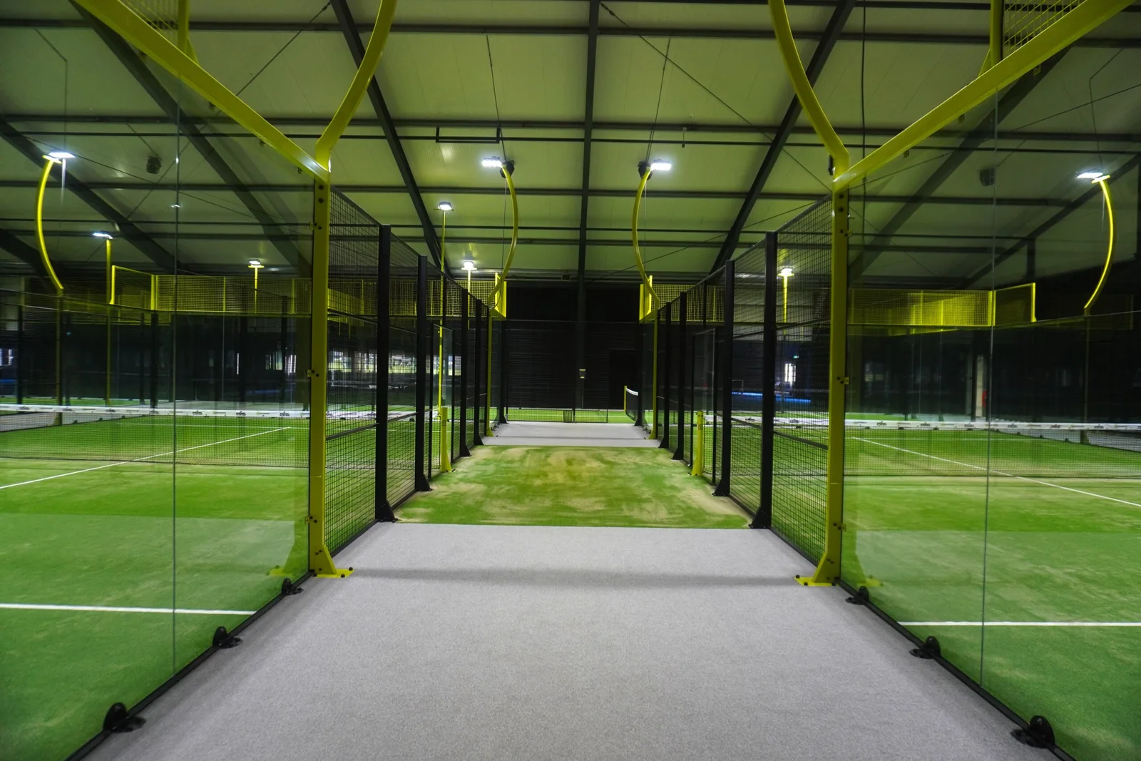 Green indoor padel courts at Padelclub Hem with yellow posts and court lighting