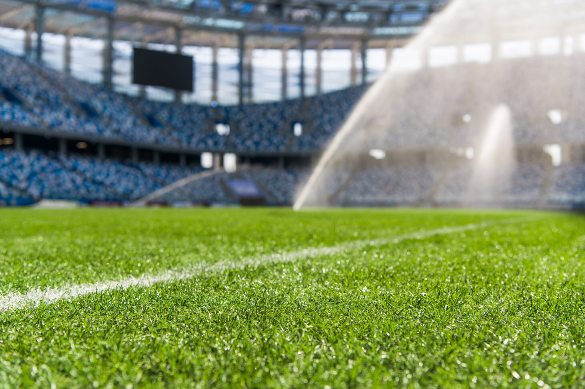 A sprinkler watering a sports pitch in an empty stadium